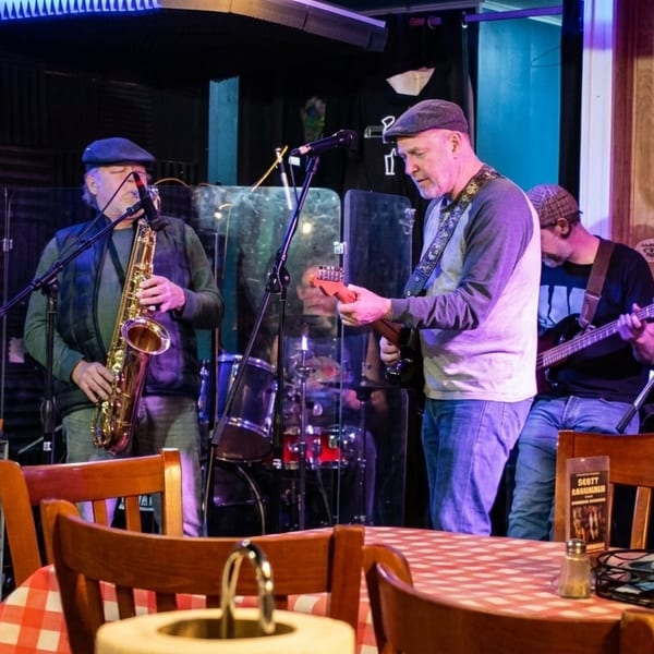 A band performs live music on a stage with red and white checkered tables in the foreground.