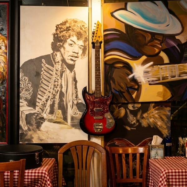 Restaurant interior with Jimi Hendrix paintings, a hanging guitar, and checkered tablecloths.