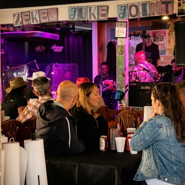 Patrons seated at tables, enjoying live music at Zeke's Juke Joint, with a "No Smoking" sign visible.