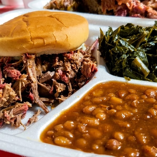 Papa Turney's BBQ pulled pork sandwich, collard greens, and baked beans in a to-go container.