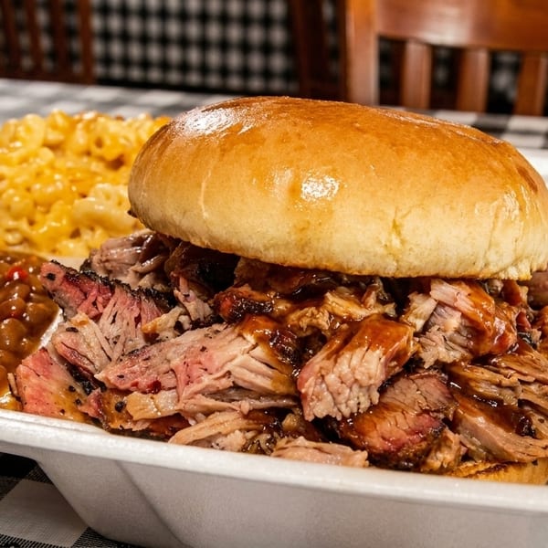 A BBQ brisket sandwich with baked beans and macaroni and cheese in a white takeout container.