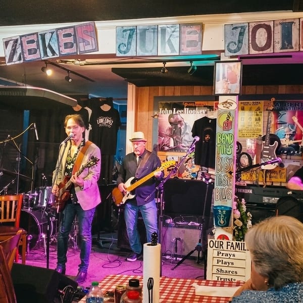 A band performs on stage at Miss Zeke's Juke Joint, with audience members seated at tables.